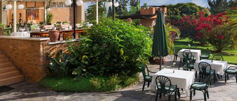 Un patio al aire libre con suelo de piedra, sillas verdes y mesas dispuestas para comer.