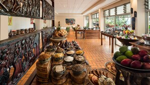 Un café amplio con diversas opciones de comida y bebida exhibidas en las mesas, rodeado de grandes ventanales que ofrecen vistas al exterior.