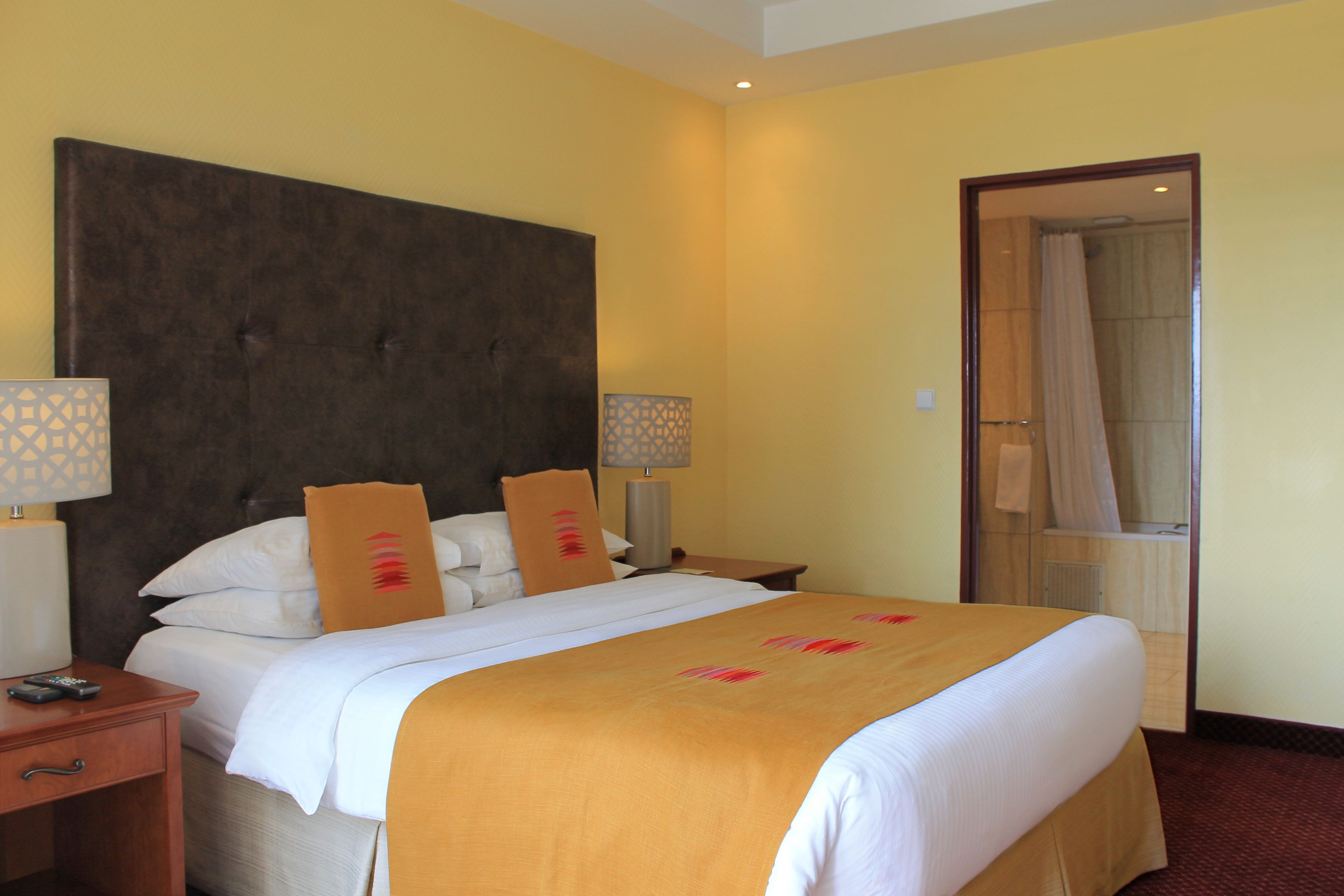 Une chambre d’hôtel avec un grand lit, deux tables de chevet, une petite table et une salle de bain visible à travers une porte ouverte.