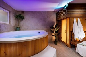 A modern bathroom with a wooden bathtub, a potted plant, and a wooden cabinet with towels.