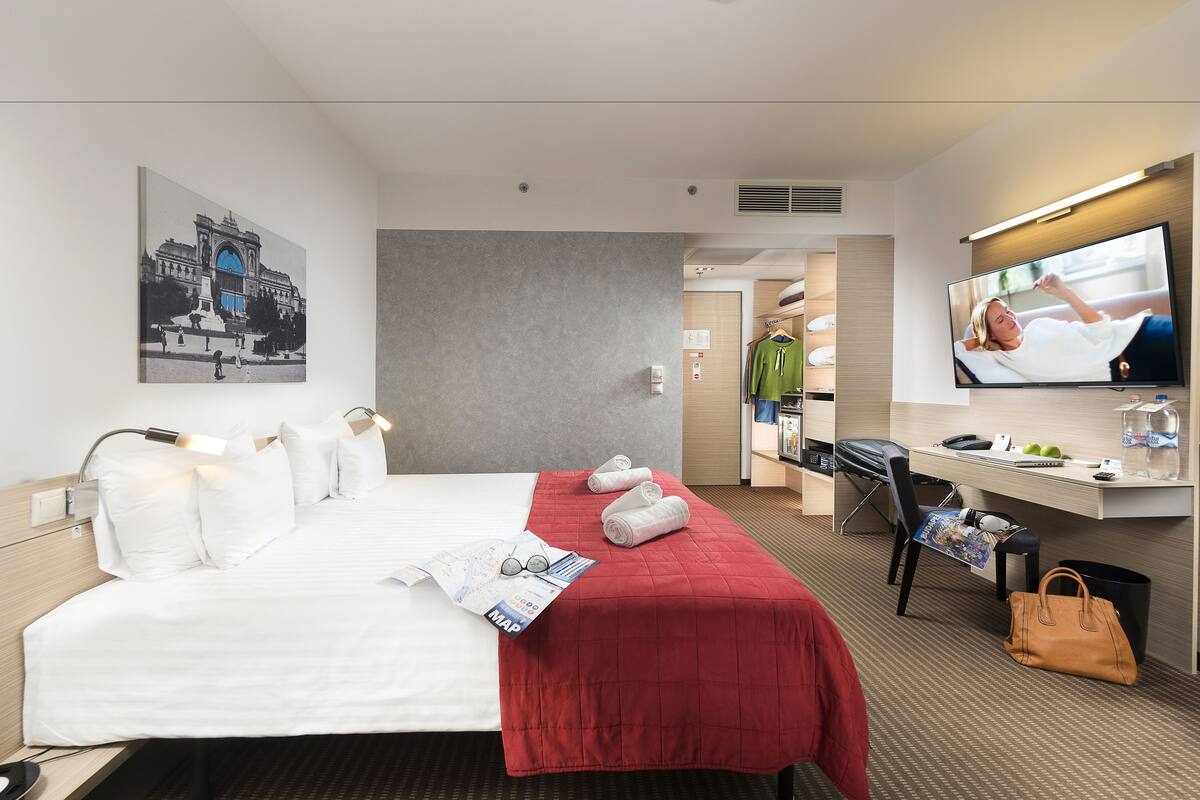 A hotel room with a bed, a desk, a TV, and a map on the bed.