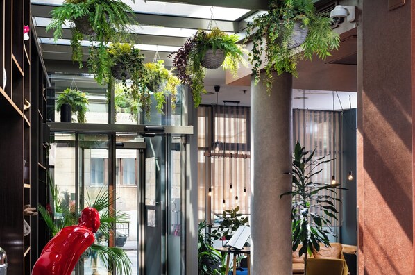 Un interior moderno con un ascensor de vidrio, plantas colgantes y una escultura roja.