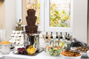 A buffet setup with a chocolate fountain, various food items, and condiments. - Bo18 Hotel Superior (Budapest)