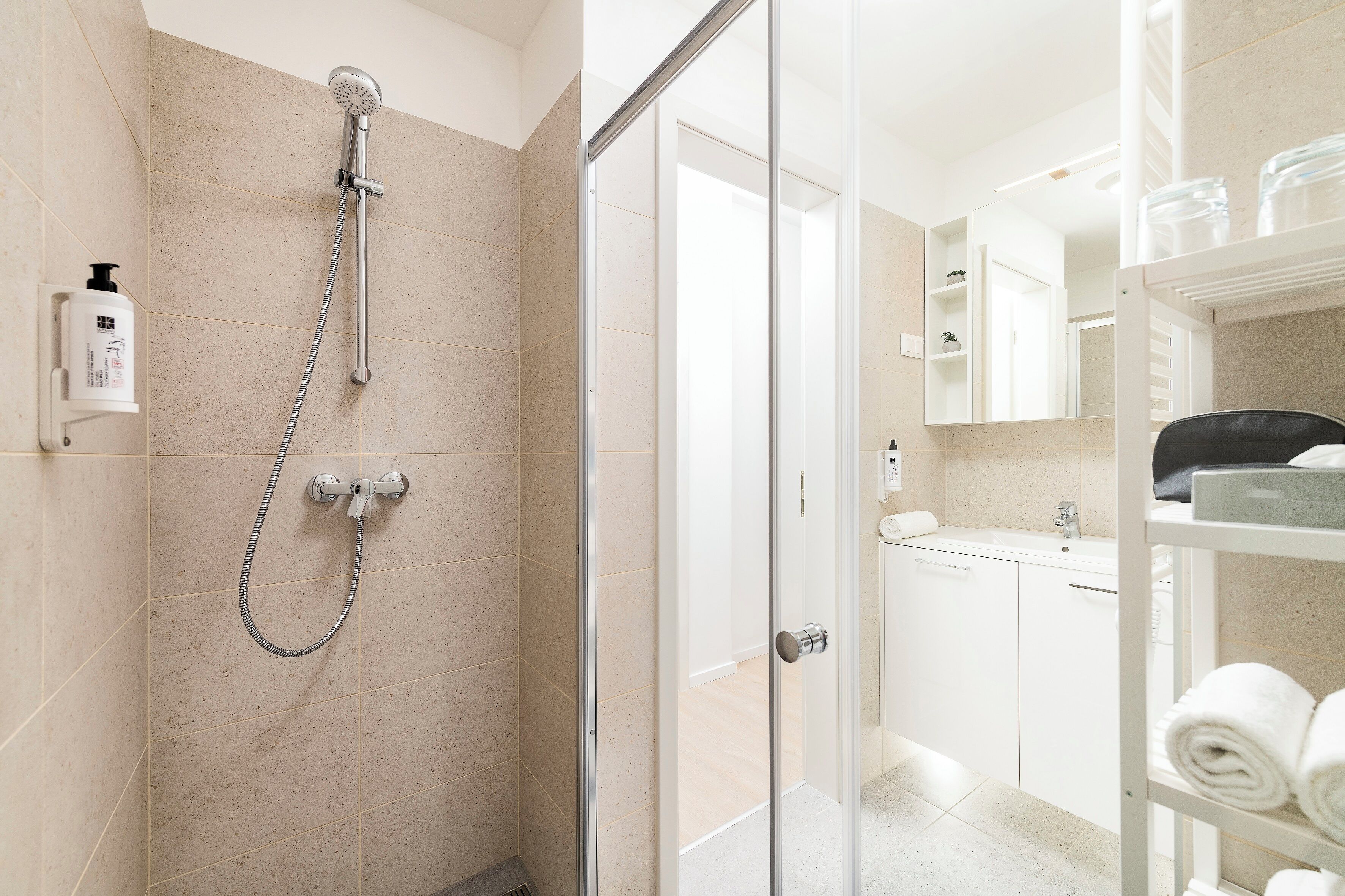 A modern bathroom with a glass shower enclosure, a white sink, and a towel rack.