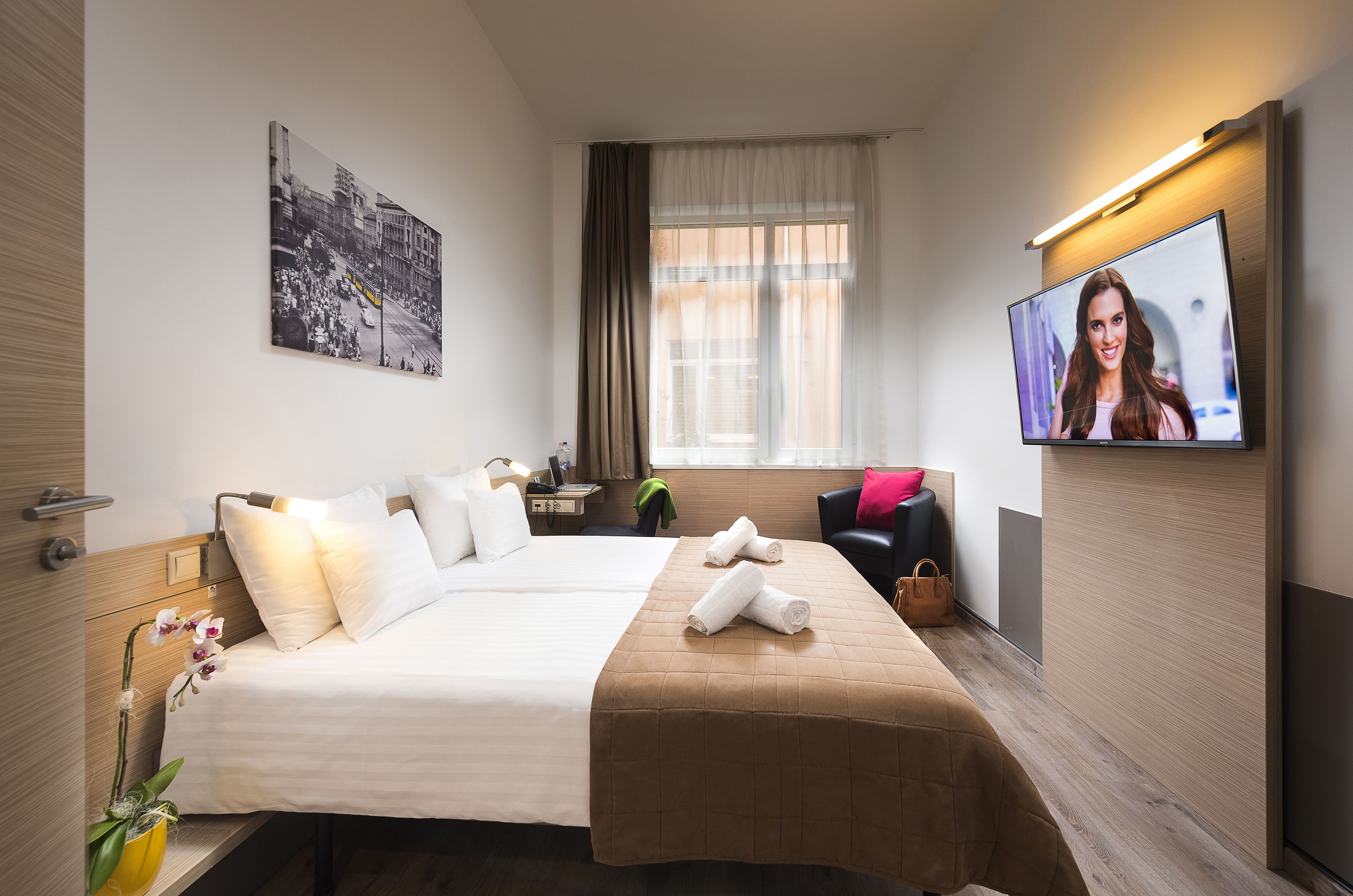 Una habitación de hotel con una cama grande, televisión, un cuadro en la pared y una ventana con cortinas.