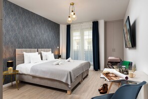 Ein modernes Hotelzimmer mit einem großen Bett, einem Nachttisch mit Lampe, einem Schreibtisch mit Stuhl, einem Korb und einem an der Wand befestigten Flachbildfernseher.