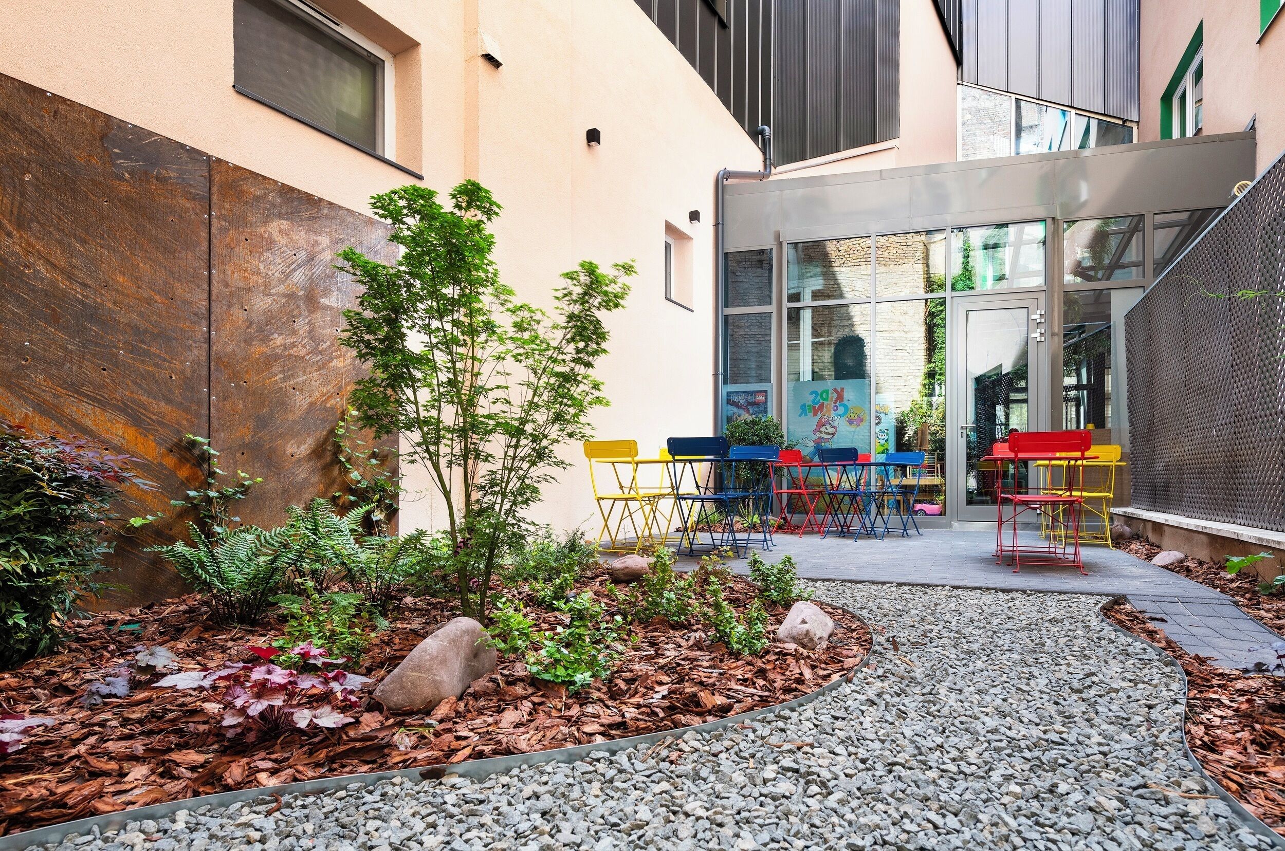 Un patio con un árbol pequeño, sillas coloridas y un sendero.