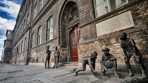 Um edifício histórico com uma porta vermelha e janelas em arco, apresentando fachada de tijolos e uma placa na parede.
