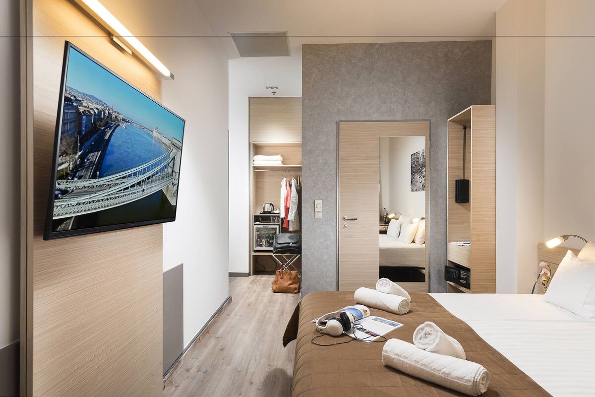 A hotel room with a bed, a TV mounted on the wall, a closet, and a bathroom with a mirror.