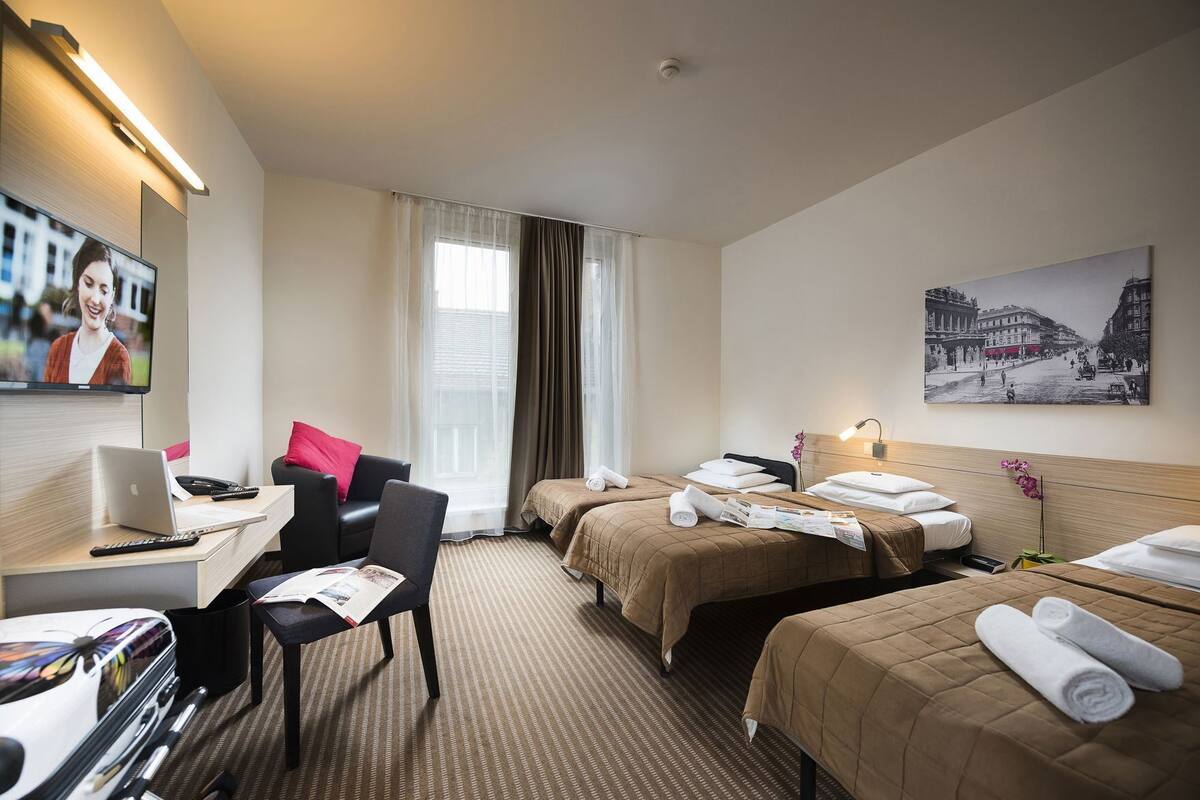 A hotel room with a desk, two beds, a TV, and a painting.