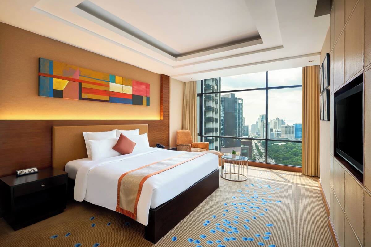 A modern hotel room with a large bed, a TV, a city view, and a decorative abstract painting on the wall.