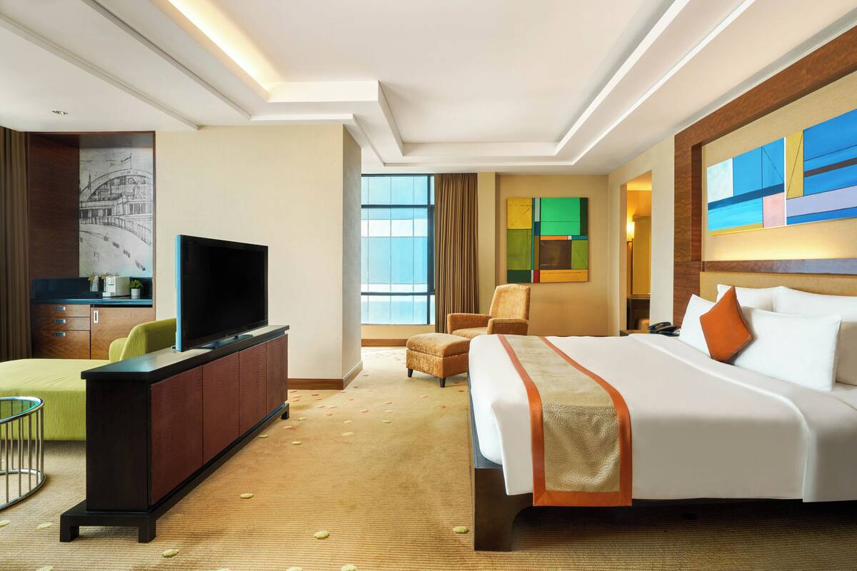 A hotel room with a large bed, a television on a cabinet, a desk with a chair, and a window with curtains.