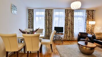 A living room with a dining area, a flat-screen TV, floral curtains, a chandelier, and a leather sofa.