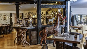 A restaurant interior with wooden tables, chairs, and a large giraffe sculpture. - Hotel Laterne (Baden-Baden)