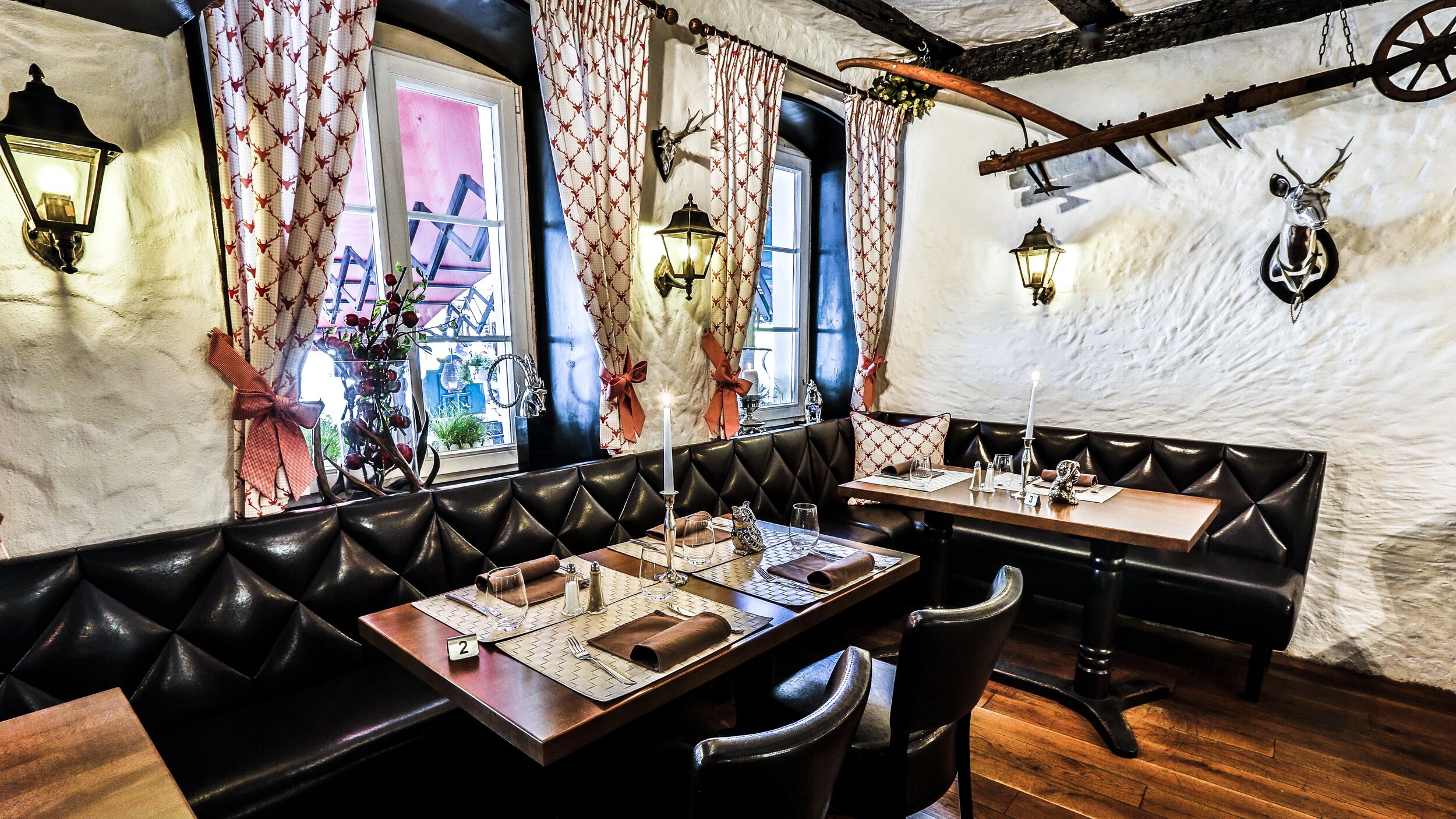 A restaurant with leather booths, wooden tables, and vintage decor including wall-mounted lanterns and a rustic ceiling.