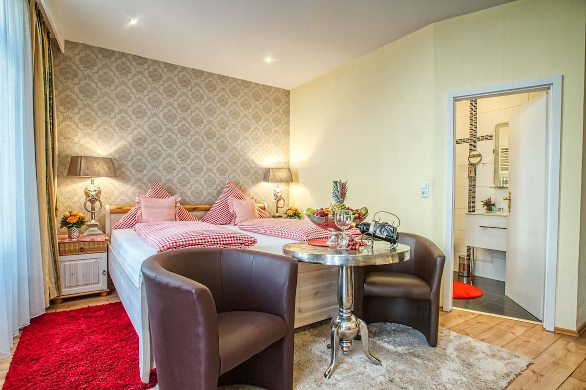 A bedroom with a bed, two bedside tables, a small round table, two chairs, and a red rug.