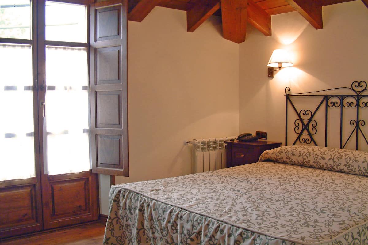 A bedroom with a bed, a nightstand, a wall-mounted lamp, and a radiator.