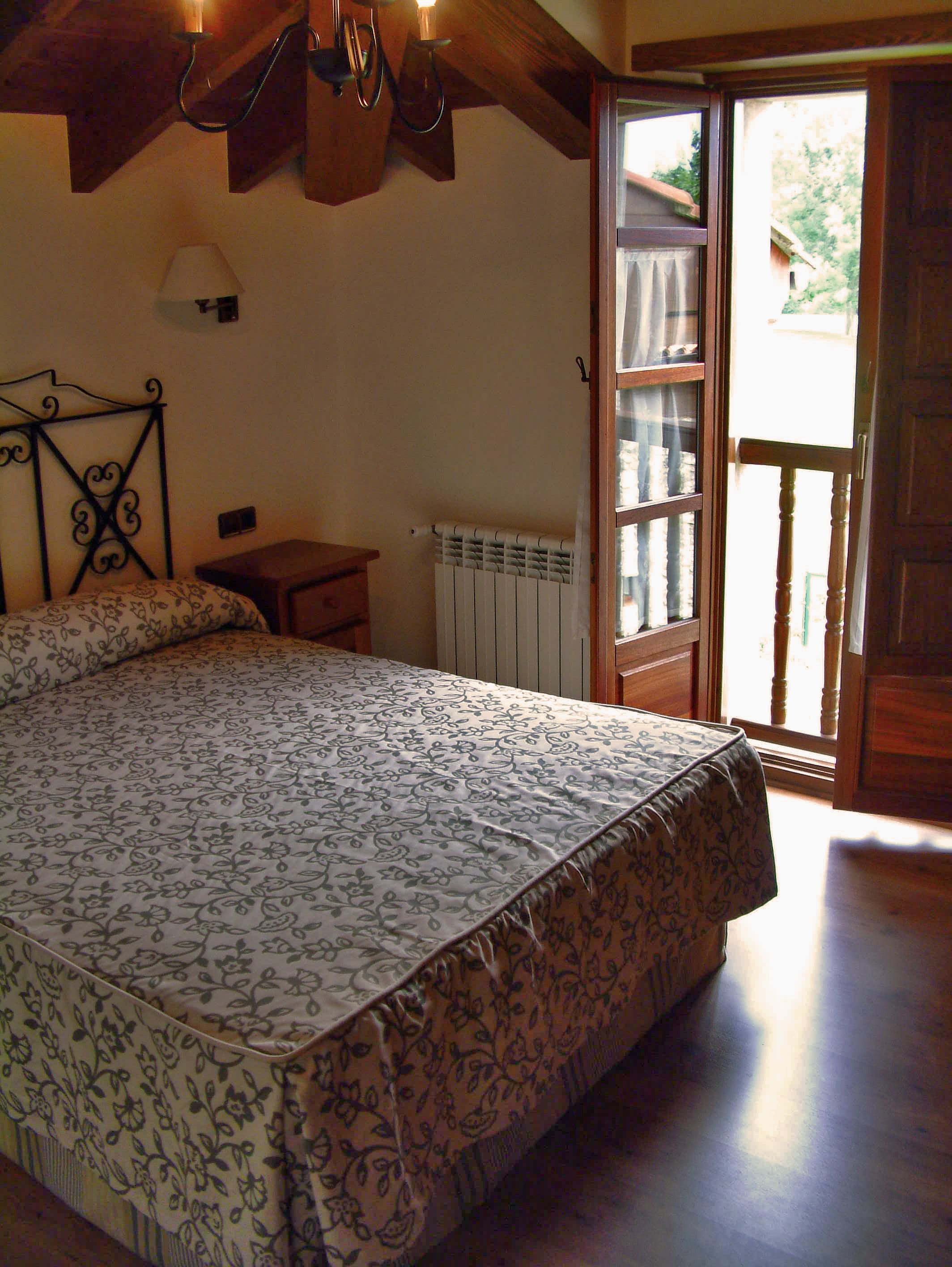 A bedroom with a bed, a nightstand, a radiator, and a wooden ceiling.