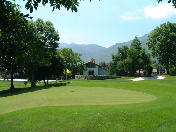 Un campo da golf con un muro di pietra, una bandiera e una casa sullo sfondo.