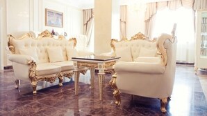 Ein luxuriöser Raum mit einem großen, aufwendig gestalteten Sofa und passendem Sessel sowie einem kleinen Tisch mit goldfarbenen Akzenten.