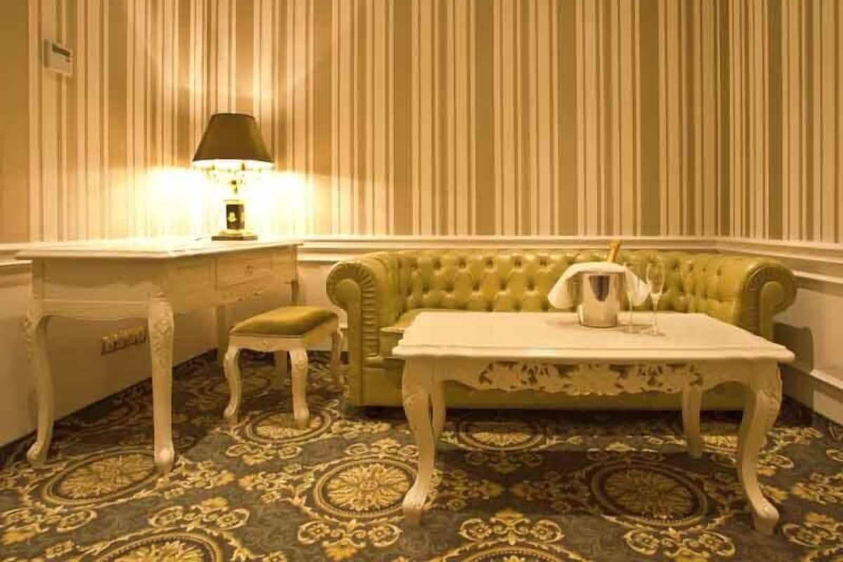 Una habitación con papel tapiz a rayas, un sofá verde, una mesa blanca y una alfombra estampada.