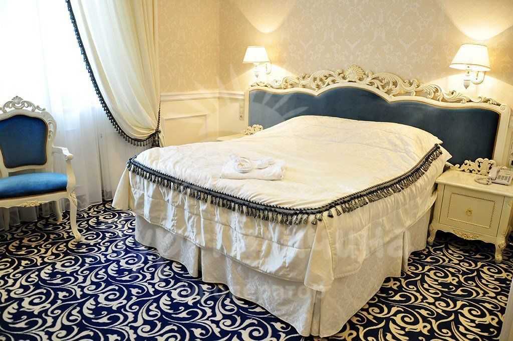 A hotel room with a large bed, two bedside lamps, a chair, and a patterned floor.
