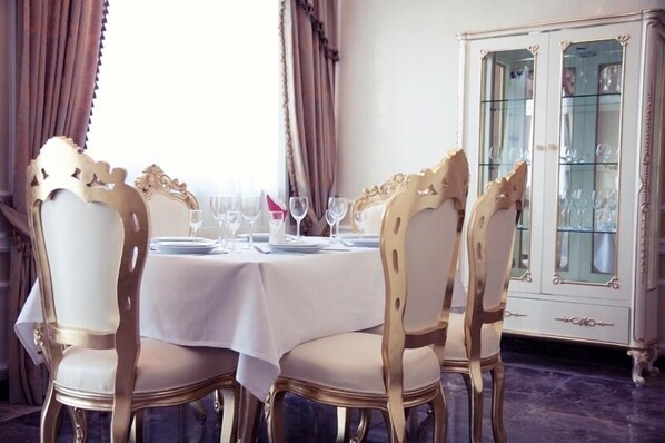 A dining area with a round table set for four, surrounded by ornate chairs with gold accents.