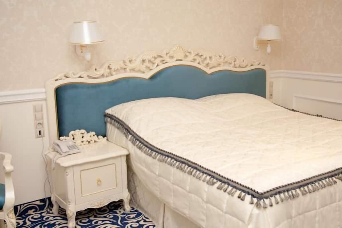 Un dormitorio con cabecera tapizada en azul, una mesita de noche blanca con una lámpara y suelo estampado.
