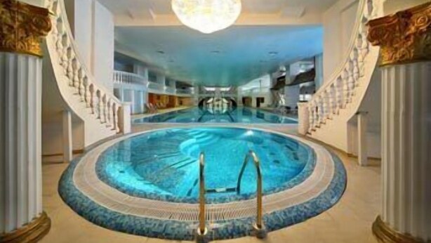 Ein großer, überdachter Pool mit einem zentralen Sprungbereich, umgeben von einer runden Liegefläche und verzierten Säulen.