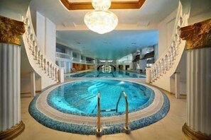 A large indoor swimming pool with a central diving area, surrounded by a circular deck and ornate columns.