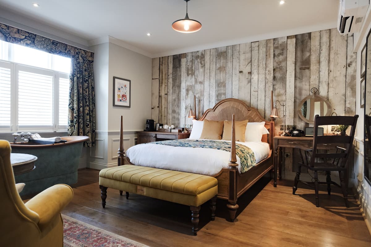 A bedroom with a wooden wall, a bed with a headboard, a desk, a chair, and a window with curtains.