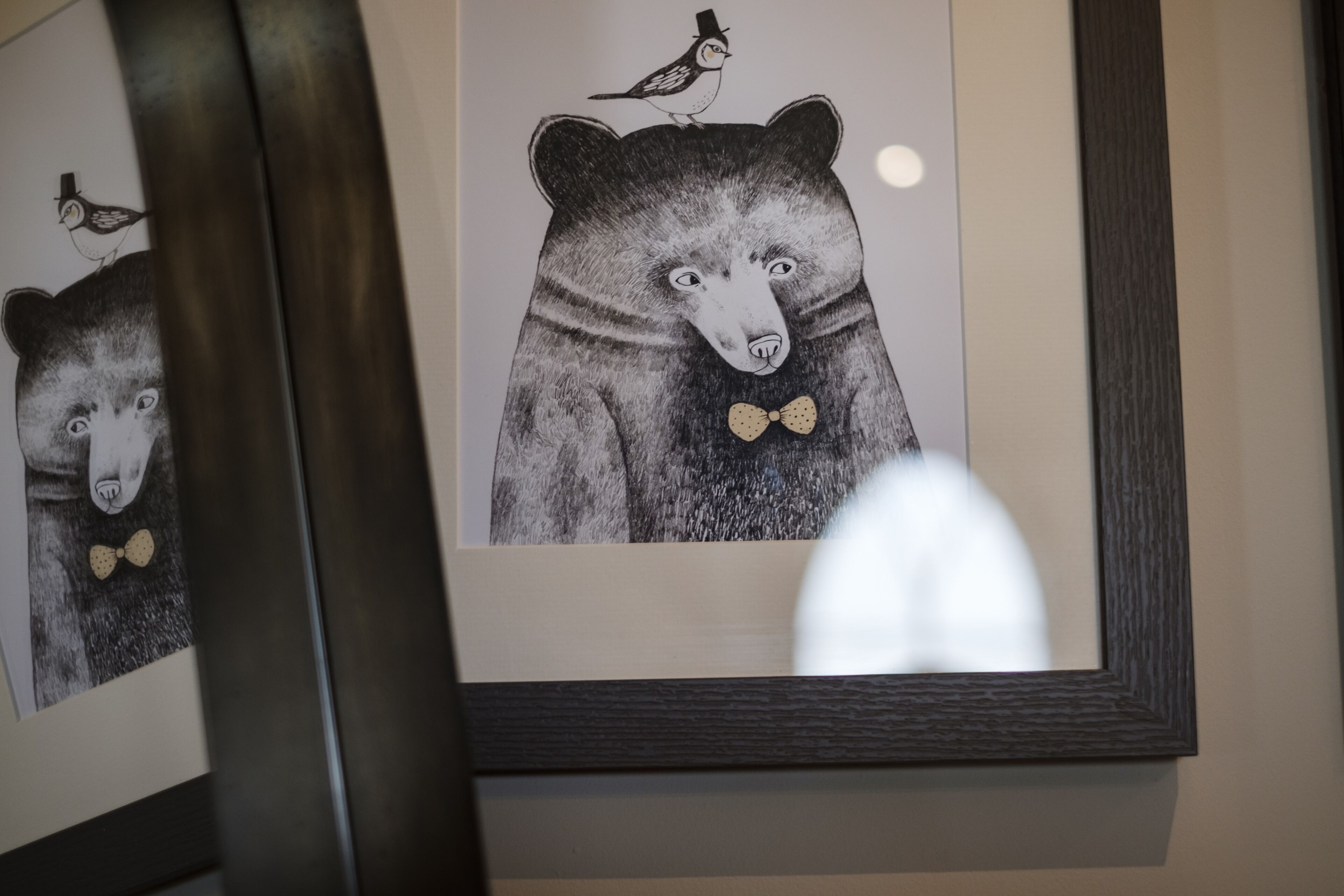 Una obra de arte enmarco que muestra un oso con corbata y un pájaro en la cabeza, expuesta en una pared.
