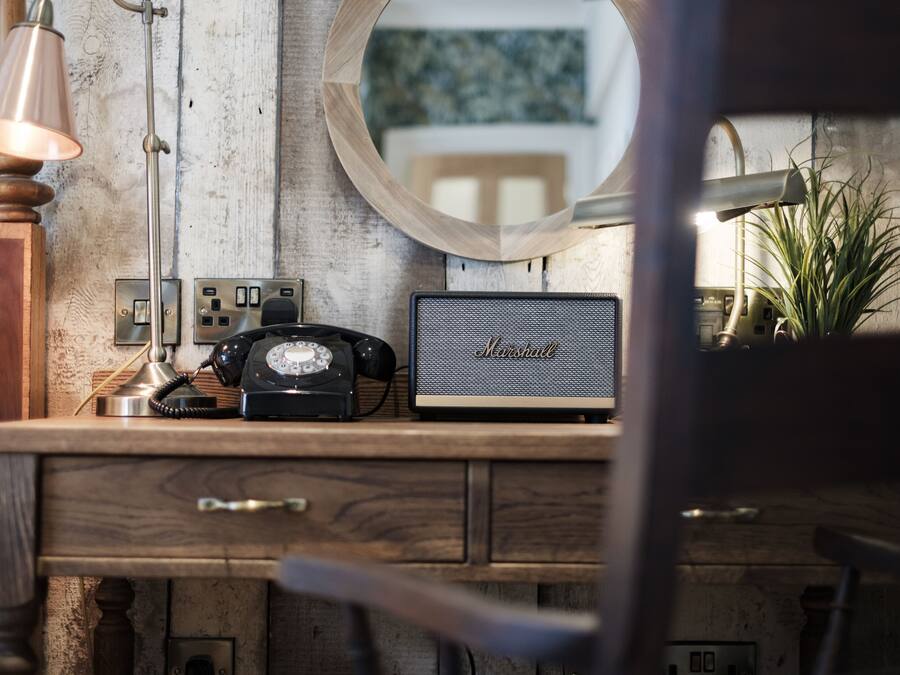 A wooden desk with a vintage telephone, a Marshall speaker, and a lamp.