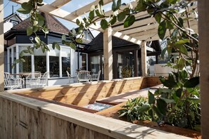 A wooden deck with a built-in seating area, surrounded by potted plants and a pergola structure. - The Bear of Burton (Christchurch)