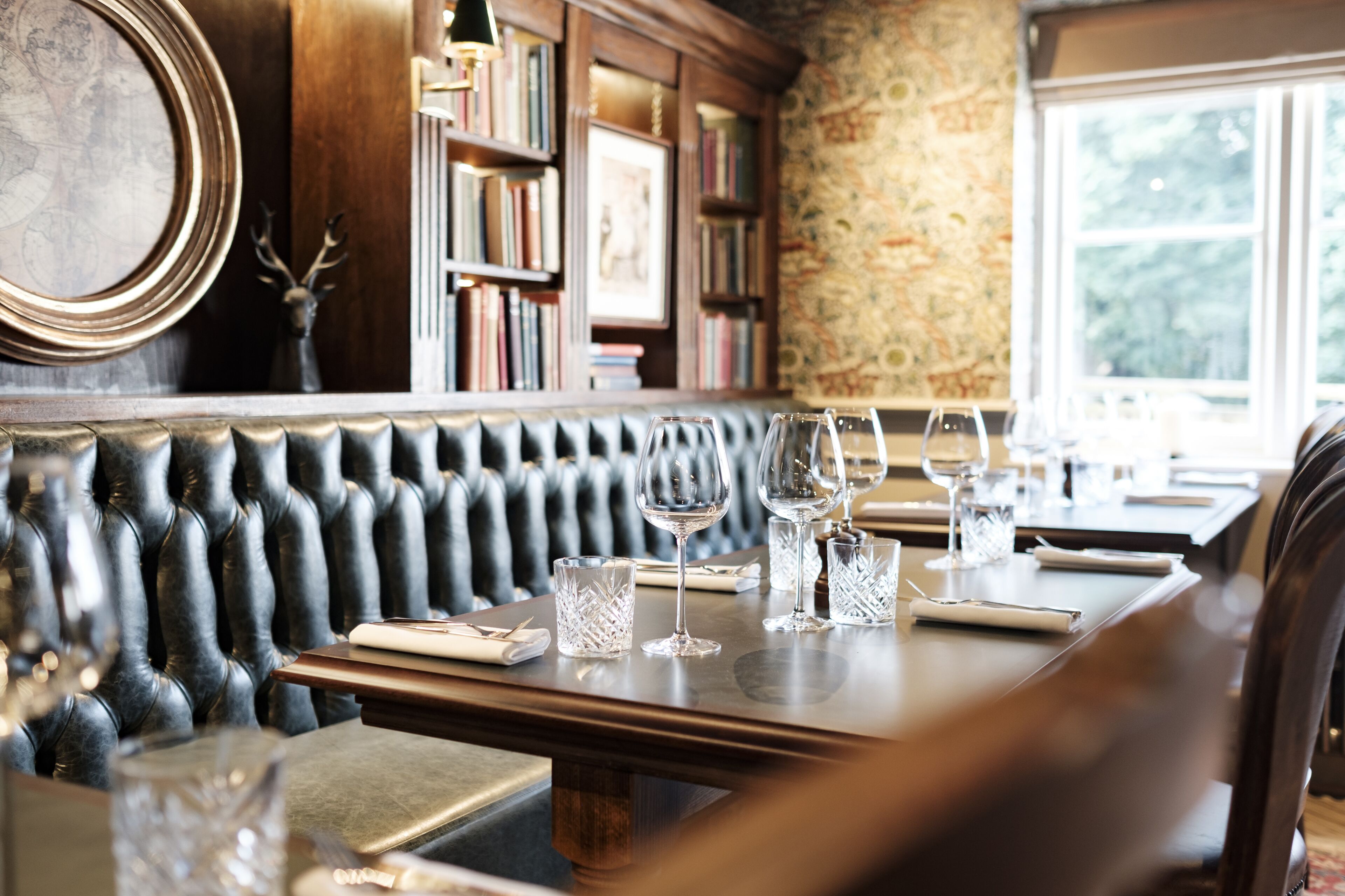 A restaurant with a leather booth seating area, wooden tables, and wine glasses.