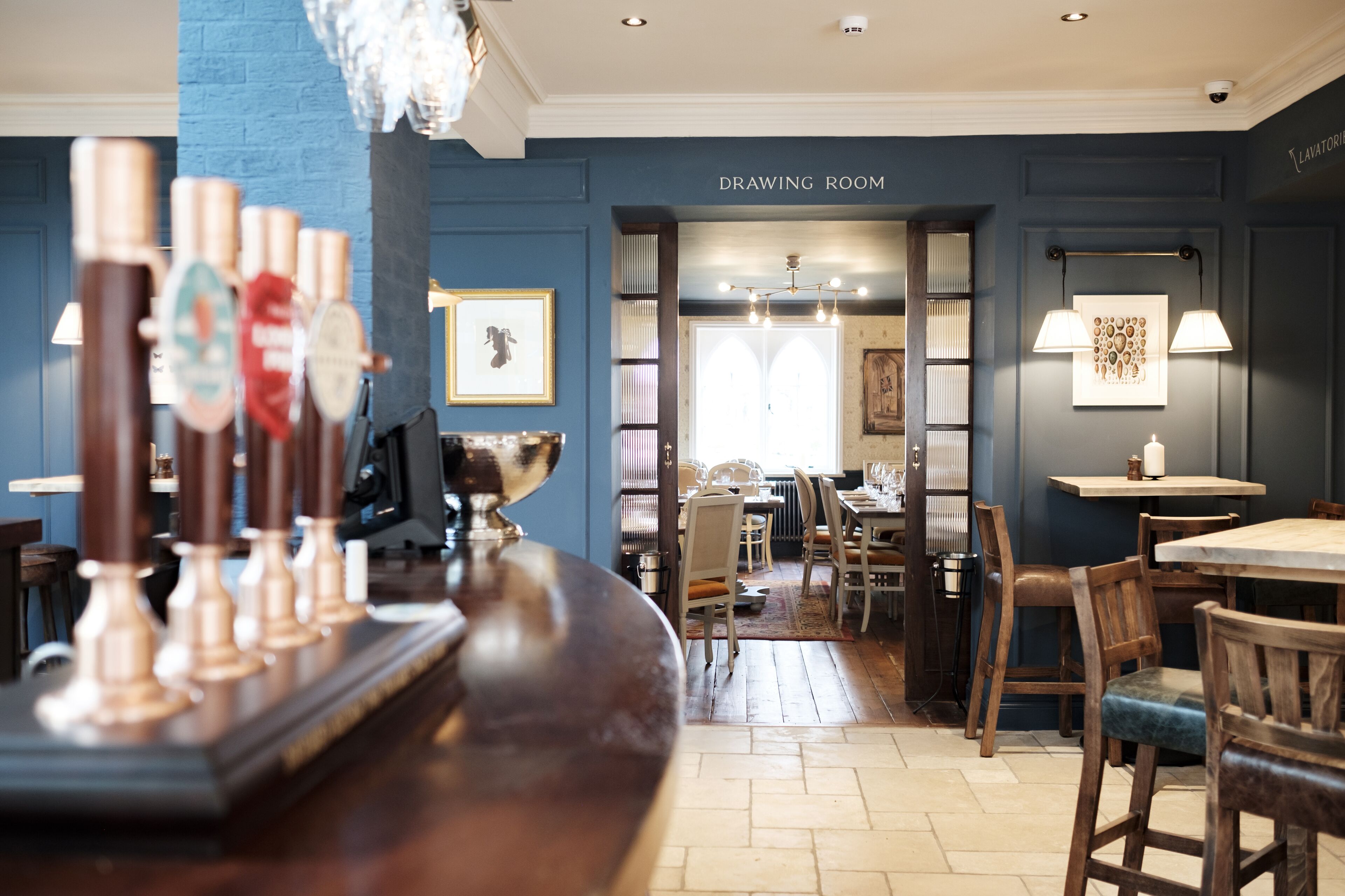 A bar area with a counter and stools, a drawing room with a table and chairs, and a sign reading "DRAWING ROOM".