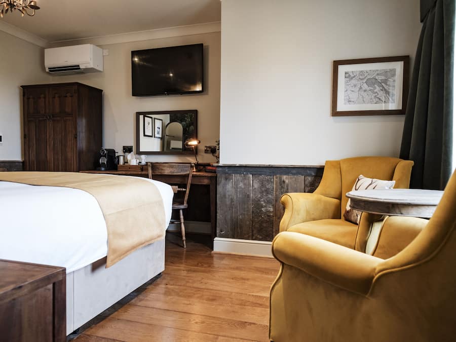 Quarto de hotel com uma cama grande, uma escrivaninha com cadeira, televisão e um quadro na parede.