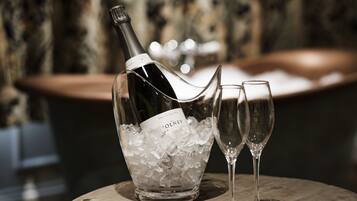 A bottle of wine in a glass container filled with ice cubes, with two empty wine glasses beside it.