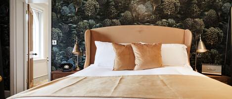 A bedroom with a large bed, a nightstand with a lamp, and a wall with a tree pattern.