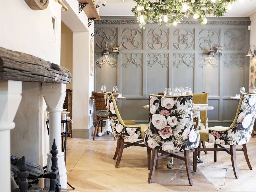 Uma área de refeições com cadeiras de padrão floral, um lustre e um painel decorativo na parede.