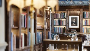 Uma biblioteca com estantes, um retrato emoldurado e uma mesa com copos.