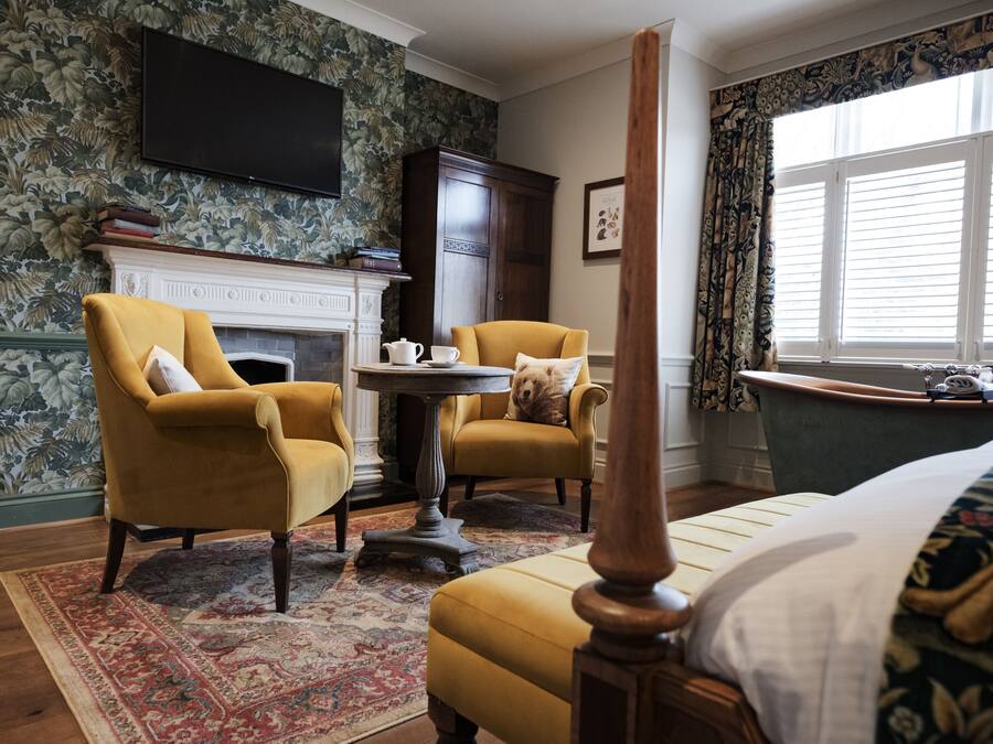 A room with a four-poster bed, a fireplace, a television mounted on the wall, and a window with curtains.