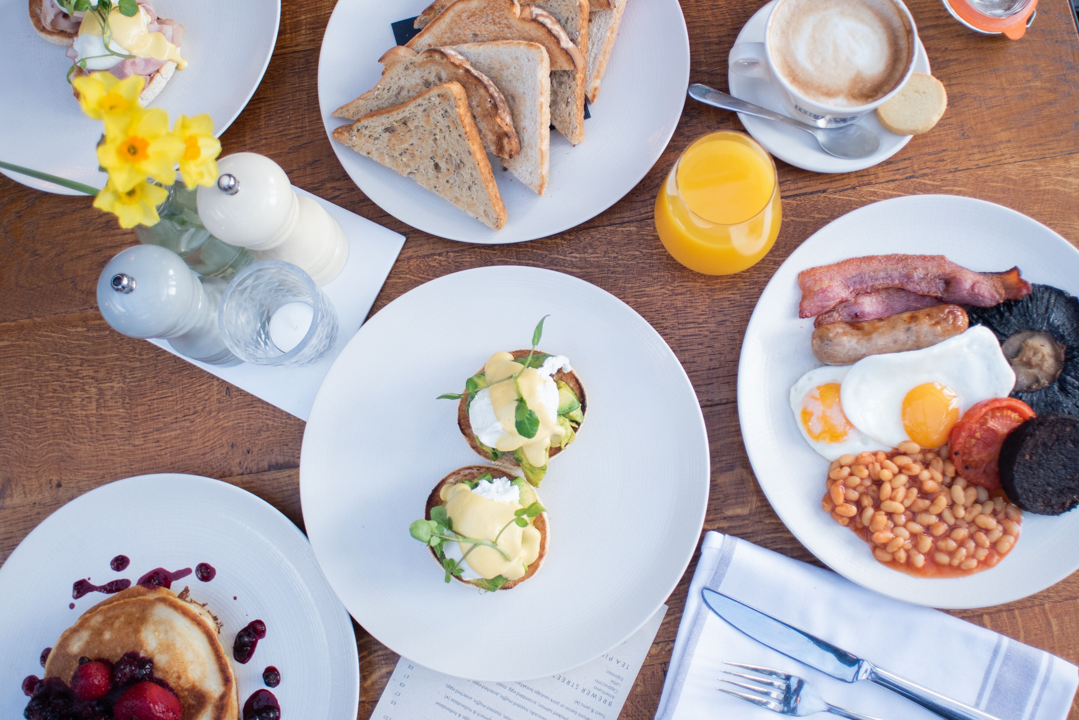 A breakfast table with various dishes including toast, eggs, sausages, and pancakes.