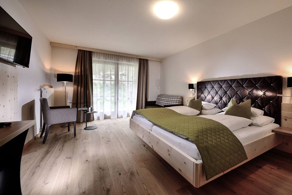 A modern hotel room with a large bed, a desk, a chair, a TV, and a window with curtains.