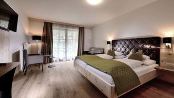 Ein modernes Hotelzimmer mit einem großen Bett, einem Schreibtisch, einem Sessel, einem Fernseher und einem Fenster mit Vorhängen.