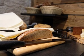 A loaf of bread on a cutting board with a knife, a basket of bread, and a loaf of cheese on a table. - Die Waldruhe (Kartitsch)