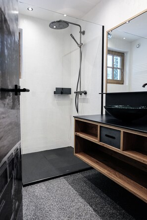 A modern bathroom with a glass-enclosed shower, a black sink, and a wooden vanity. - Die Waldruhe (Kartitsch)