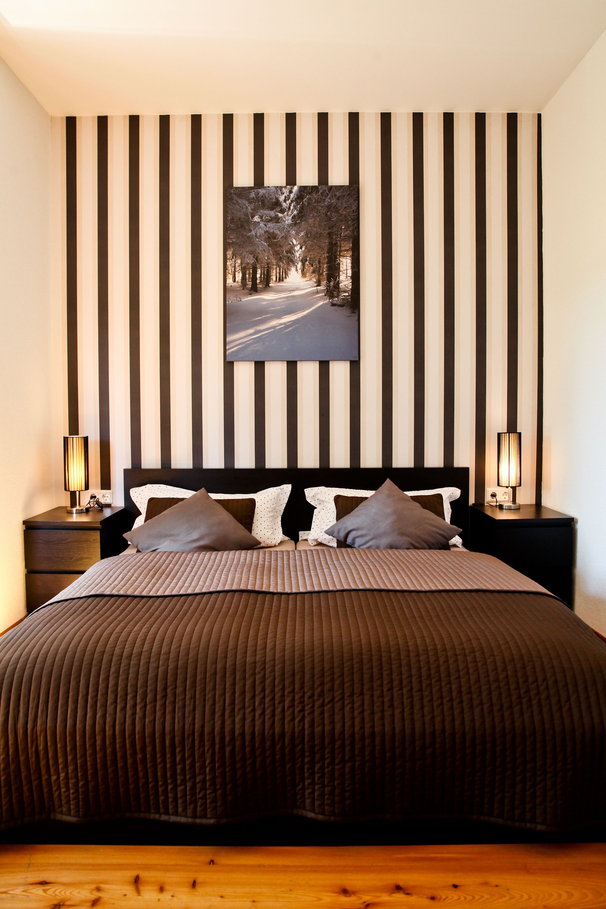 A bedroom with a large bed, striped wall panels, a framed picture, and two bedside lamps.