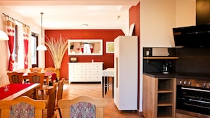 A modern kitchen with a built-in oven, a dining area with wooden chairs and a red table runner, and a white refrigerator. - Oberhof 810 M (Oberhof)