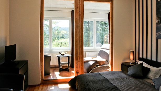A bedroom with a large bed, a TV, a desk, and a chair. There is a window with a view of trees and a balcony. - Oberhof 810 M (Oberhof)